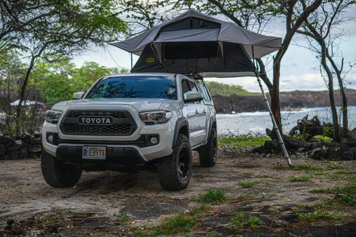 White Toyota Tacoma with a gray rooftop tent set up for coastal camping on Hawaii's lava rocks. Your adventure RV rental.. Custom Camper 2016