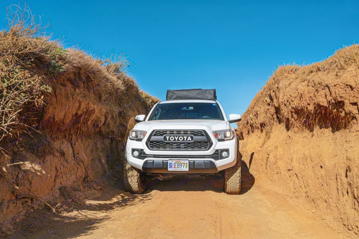 A white Toyota Tacoma navigates a narrow, dry dirt path. This robust truck is an ideal vehicle for a thrilling RV rental adventure.. Custom Camper 2016