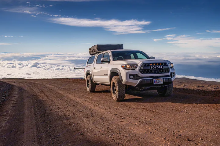 White Toyota Tacoma with rooftop tent on a high mountain dirt road, above the clouds. Ultimate adventure, like an RV rental for rugged travel.. Custom Camper 2016