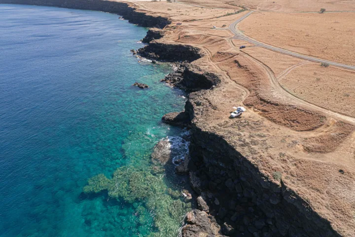 Aerial view: A white RV rental truck with a rooftop tent on a dry cliff overlooking the clear blue ocean.. Custom Camper 2016