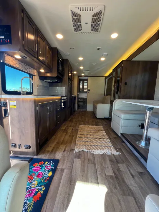 Spacious RV rental interior with full kitchen, dining booth, and living area, featuring wood floors and bright lighting.. Jayco Redhawk 2021
