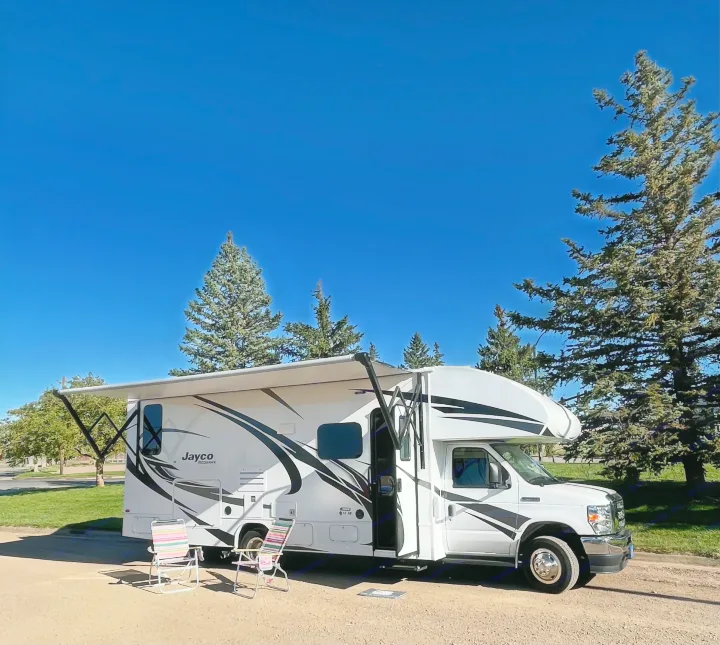 White Jayco Redhawk RV rental with extended awning and two lounge chairs set up for a sunny day of camping.. Jayco Redhawk 2021