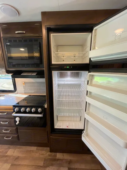 Modern RV rental kitchen with an open, empty refrigerator, microwave, and stovetop. Clean and ready for your next journey.. Jayco Redhawk 2021