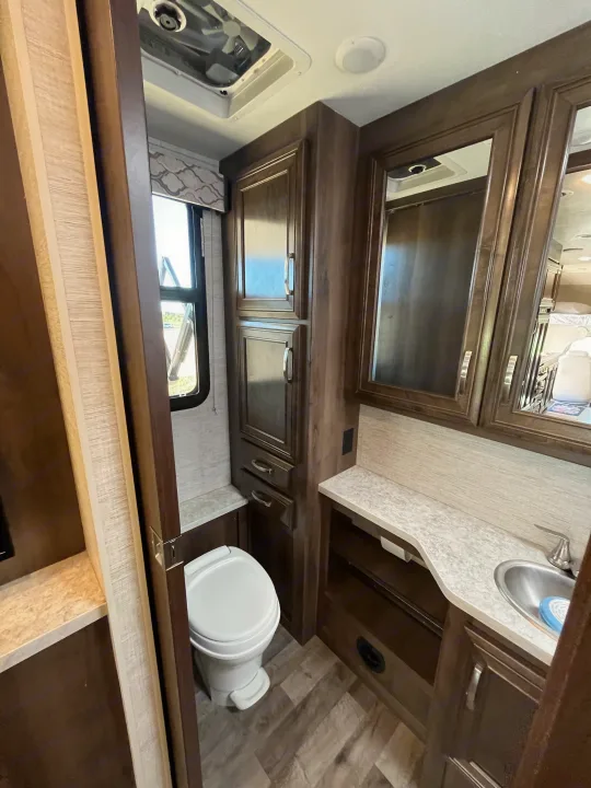 Inside an RV rental bathroom featuring a compact toilet, window, vanity with sink, mirrored cabinets, and a ceiling vent.. Jayco Redhawk 2021