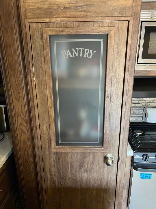 **RV rental** kitchen showcases a wooden pantry door with a frosted glass insert, clearly labeled "PANTRY," next to a microwave and stove.. Keystone RV Cougar 2017