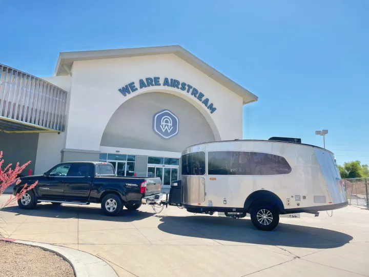 Black truck towing a shiny Airstream travel trailer, an RV rental favorite, outside the Airstream building.. Airstream Basecamp 2021