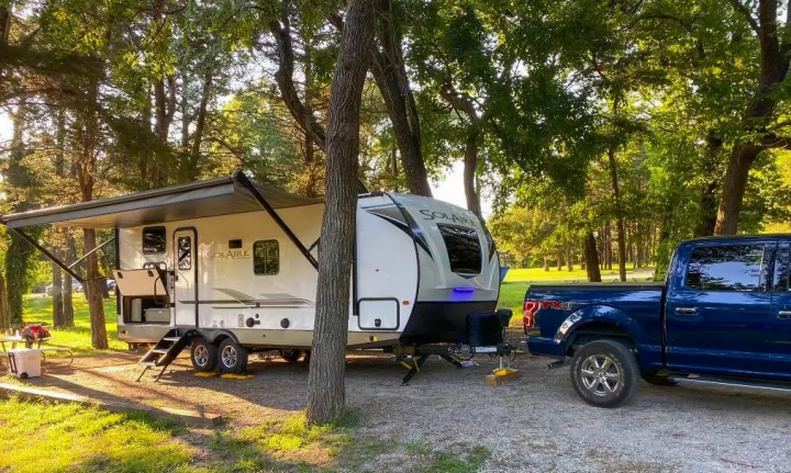 This Solaire RV rental, hitched to a blue pickup truck, is set up at a shaded campsite, perfect for your outdoor escape.. Palomino Solaire Ultra Lite 2021