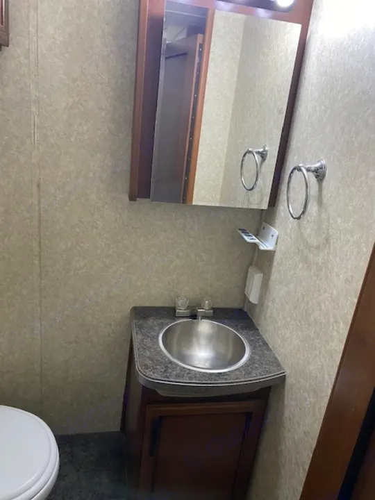 Compact RV rental bathroom features a stainless steel sink, large mirror, and partial view of the toilet, typical for campers.. Tioga Fleetwood 2011