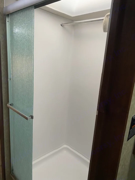 Inside a clean RV rental shower: white walls, a compact design, and a textured glass door.. Tioga Fleetwood 2011