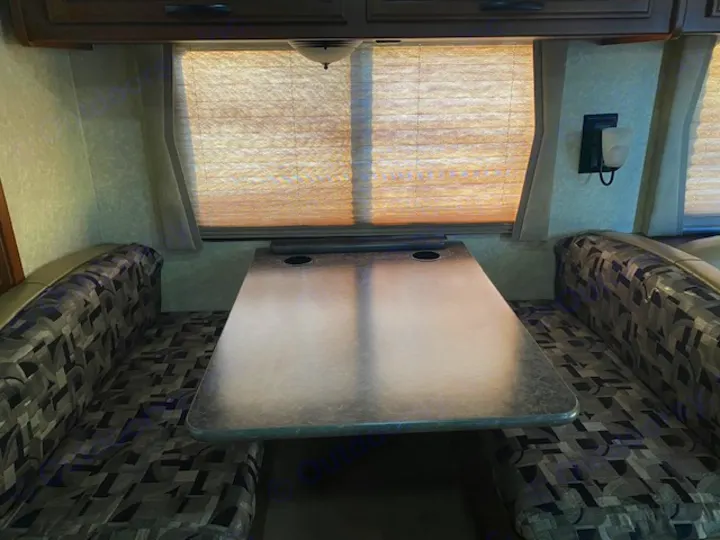 RV rental dinette interior with a table, two patterned upholstered benches, and windows with pleated shades, ideal for meals and relaxation.. Tioga Fleetwood 2011
