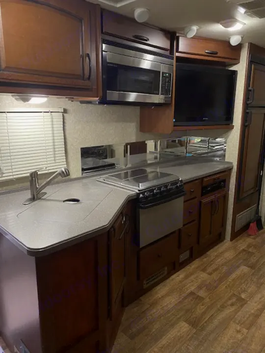 RV rental interior: kitchen with sink, stovetop, microwave, TV, and wood-toned cabinets/flooring.. Tioga Fleetwood 2011