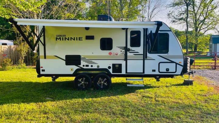 White Micro Minnie travel trailer with awning extended. Perfect for an RV rental getaway, parked on green grass.. Winnebago Micro Minnie 2021