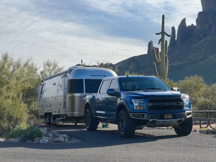 A blue Ford pickup tows an Airstream travel trailer in a desert camp. Mountains & saguaro cactus frame this ideal RV rental scene.. Airstream International 2017