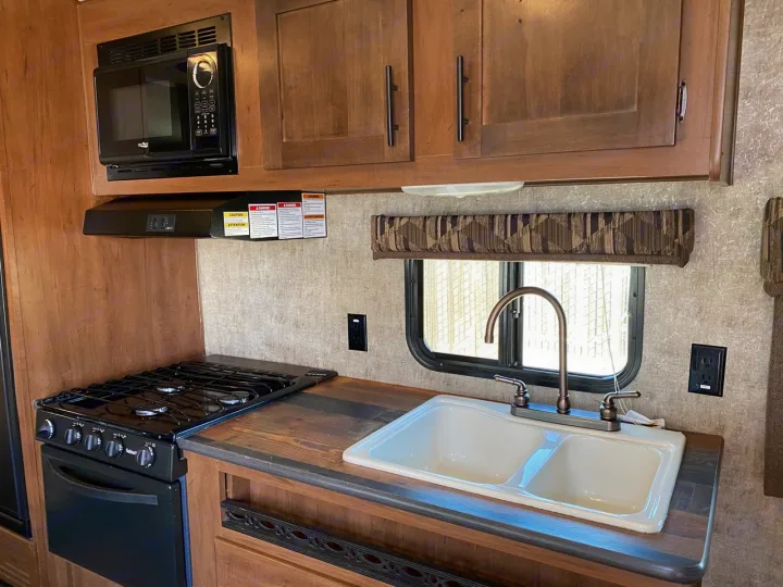 RV rental kitchen: Features a black microwave, gas stove, oven, double sink, and wood-grain cabinets for comfortable travel.. Outdoors RV Blackrock 2017