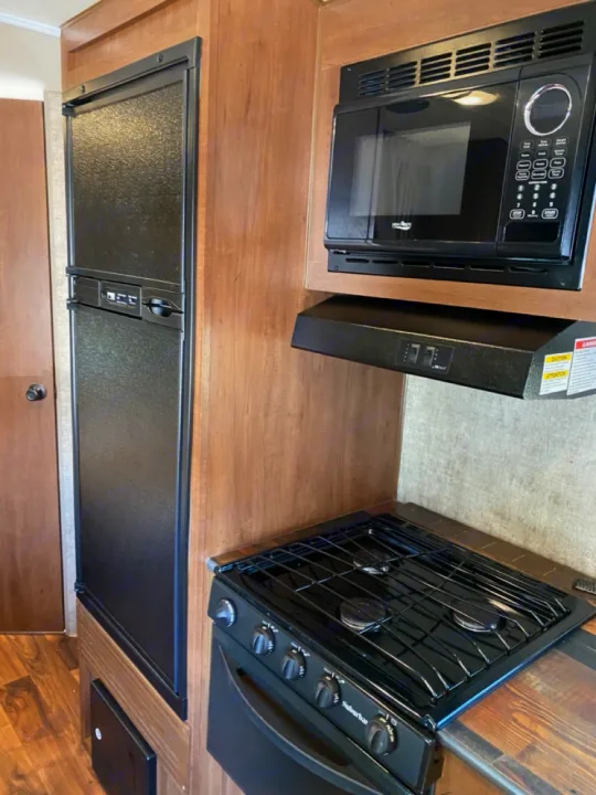 RV rental kitchen: compact with black refrigerator, microwave, and gas range in light wood cabinetry.. Outdoors RV Blackrock 2017