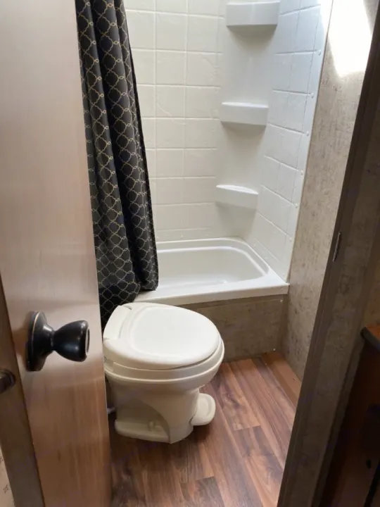 Compact RV rental bathroom: white toilet, small tub with patterned shower curtain. Ideal for travel comfort.. Outdoors RV Blackrock 2017