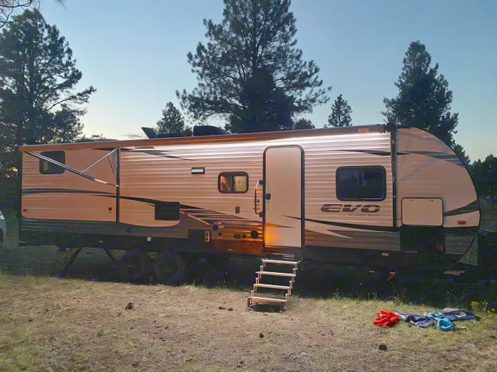 Illuminated RV rental at dusk, parked in a forested campsite with steps leading to the door.. Forest River Evo 2020