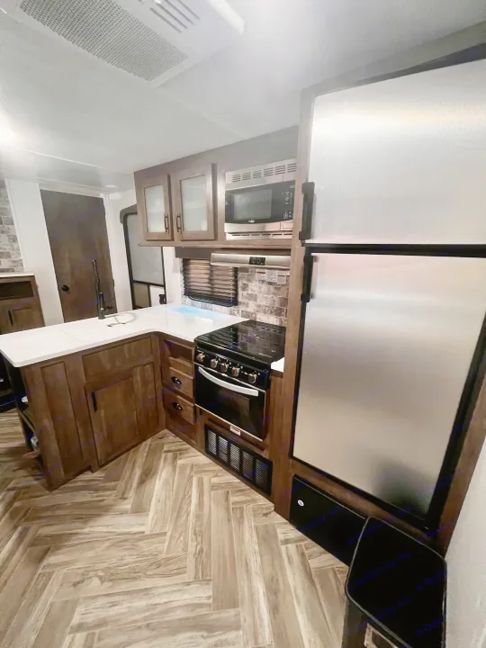 RV rental kitchen with stainless steel appliances, modern cabinets, white countertops, and herringbone flooring.. Forest River Evo 2020