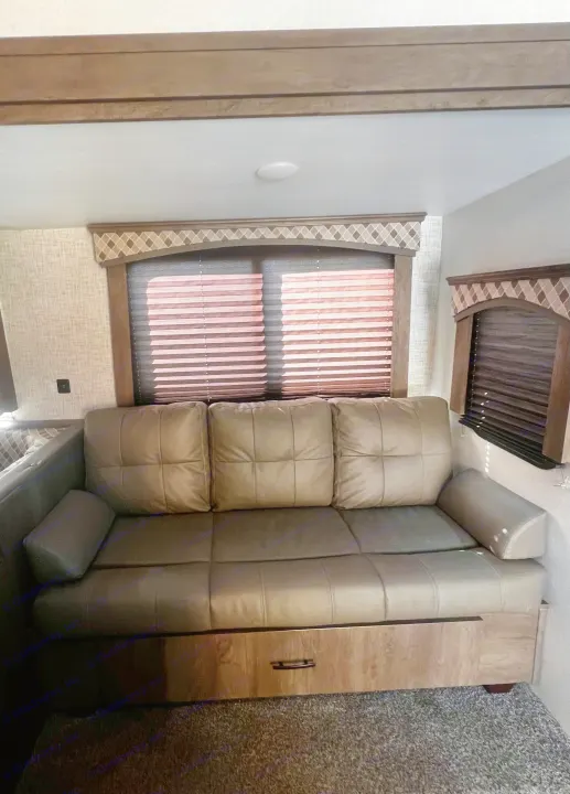 This RV rental's inviting living area features a light-colored sofa (possible pull-out), windows with blinds, and decorative valances.. Forest River Evo 2020
