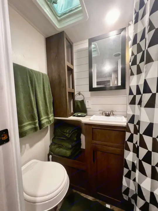Compact and well-equipped RV rental bathroom, featuring a toilet, sink, mirror, and a geometric shower curtain.. Forest River Evo 2020