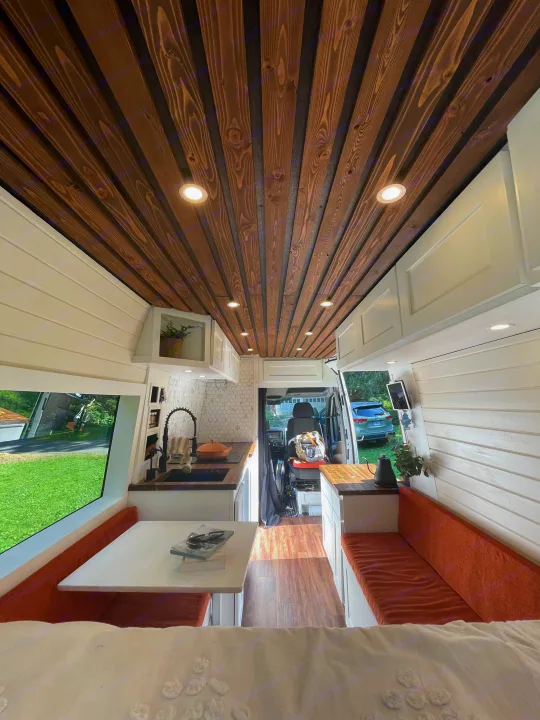 Inside a stylish RV rental: modern camper van interior features a kitchen, dining nook, and warm wood-slat ceiling.. Mercedes Sprinter 2013