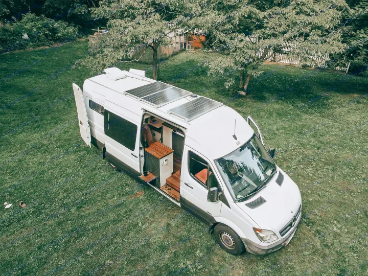White camper van with solar panels & open side door revealing interior, parked on grass. An ideal rv rental for mobile living.. Mercedes Sprinter 2013