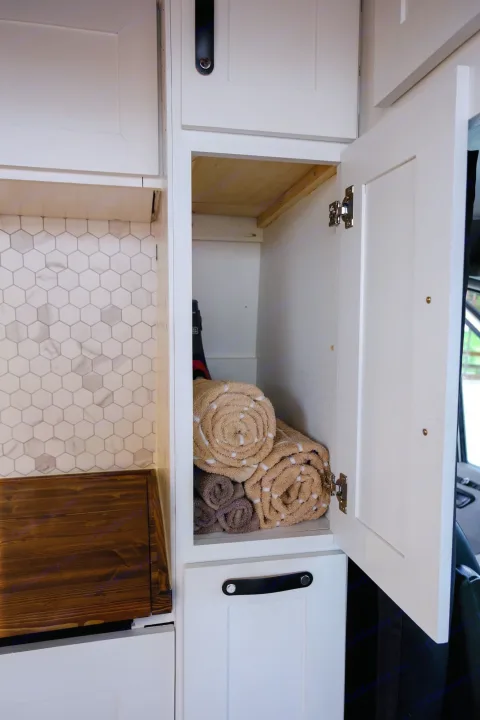 Efficient RV rental storage: Open cabinet shows rolled towels, neat kitchen area with hexagonal tile backsplash.. Mercedes Sprinter 2013
