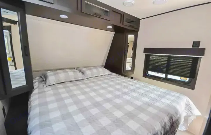 Spacious RV rental bedroom with checkered bed, overhead cabinets, and window. Perfect for your next adventure.. Jayco Jay Flight 2022