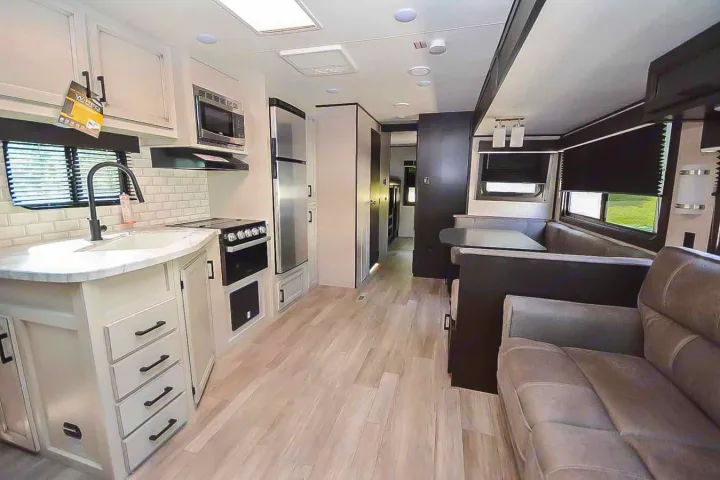 Modern RV rental interior features a well-equipped kitchen, light wood-look floors, a dining booth, and sofa.. Jayco Jay Flight 2022