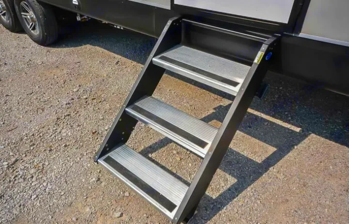 Three black and silver RV rental steps firmly planted on a gravel surface next to a travel trailer.. Jayco Jay Flight 2022