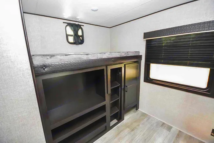 RV rental bunk bedroom: a top bed, dark wood built-in storage (shelves & cabinet), and two windows.. Jayco Jay Flight 2022