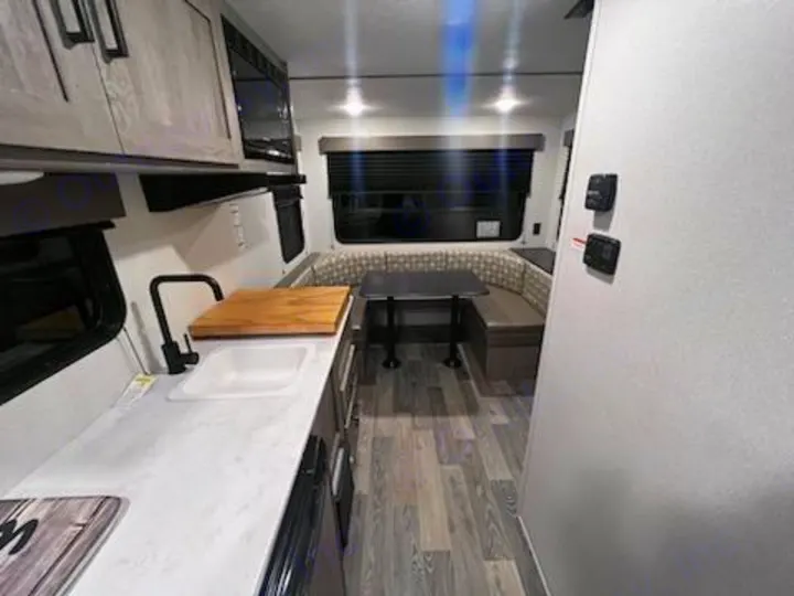 RV rental interior showcasing a bright kitchenette with sink & microwave, U-shaped dinette, and wood-look floor.. Keystone RV Springdale 2021