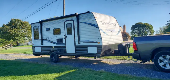A light grey & white Springdale travel trailer (RV) is hitched to a pickup truck on a gravel drive. Ready for your RV rental adventure.. Keystone RV Springdale 2021