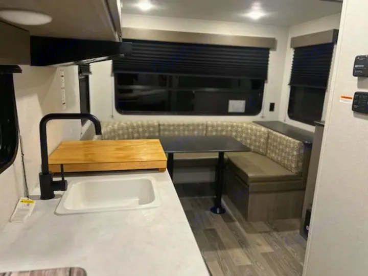 Spacious RV rental interior features a functional kitchen with sink & cutting board, plus a comfortable dining booth.. Keystone RV Springdale 2021