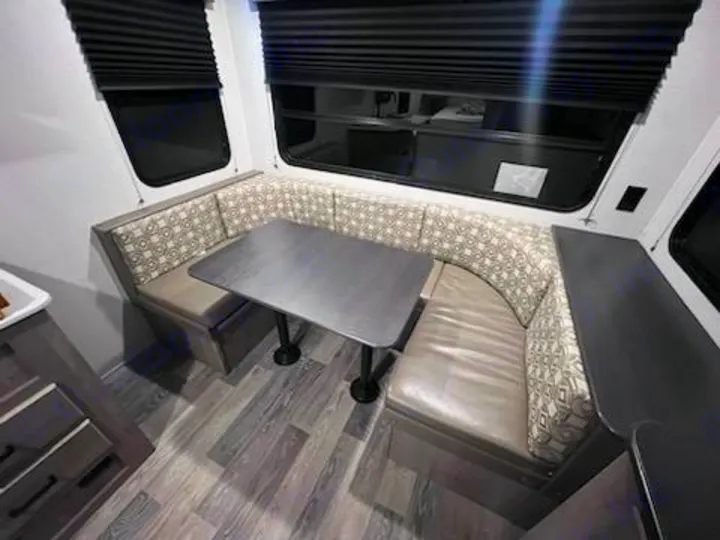 Inside an RV rental: U-shaped dinette with table, patterned cushions, large windows, and a counter.. Keystone RV Springdale 2021