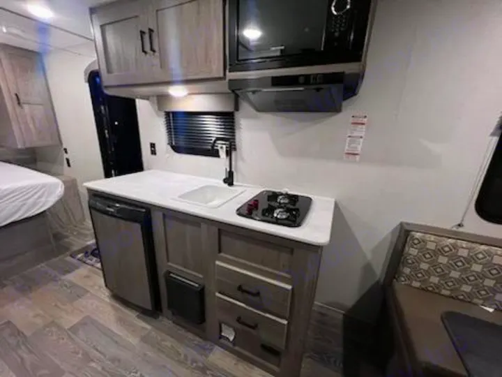 RV rental interior. View of compact kitchenette with sink, stove, fridge, microwave, plus a bed and dinette seating.. Keystone RV Springdale 2021