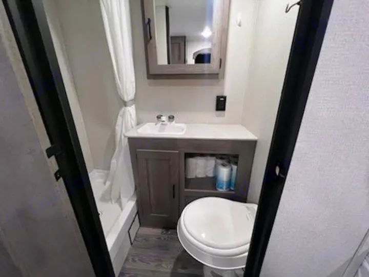 View of a compact RV rental bathroom, showing a shower, vanity, toilet, and storage.. Keystone RV Springdale 2021