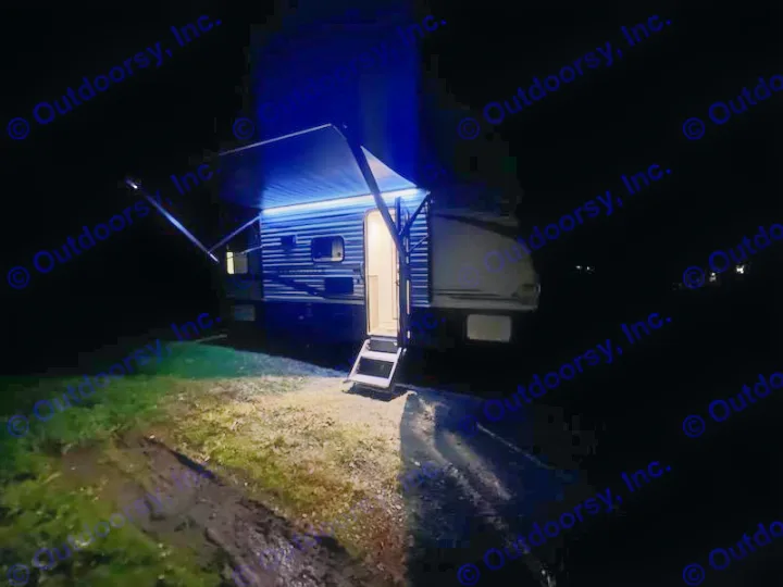 Night view of an RV rental with its awning extended and blue LED lights on, steps lit. Ideal for a serene camping getaway.. Keystone RV Springdale 2021