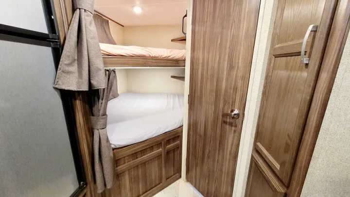 Cozy RV rental interior featuring two bunk beds with privacy curtains and wooden accents, perfect for family adventures.. Coachmen Apex 2018