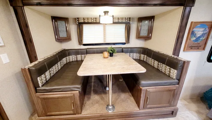 Inside an RV rental: a U-shaped dinette with dark brown seating, a light speckled table, and overhead cabinets for storage.. Coachmen Apex 2018
