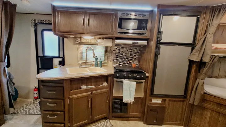 Inside an RV rental, a functional kitchen with sink, microwave, stove, and fridge, ready for your road trip.. Coachmen Apex 2018