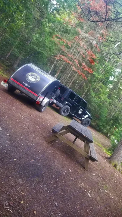 Black Jeep and teardrop RV rental trailer at a wooded campground, next to a wooden picnic table.. The Teardrop Trailer Diamond in the rough 2021