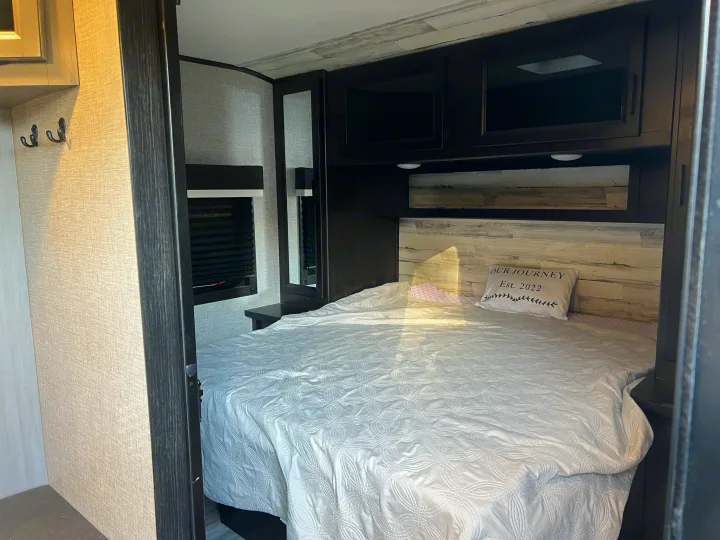 Experience comfort in this RV rental bedroom with cozy bed, stylish headboard, and ample storage, ideal for travel.. Jayco Jay Feather 2022