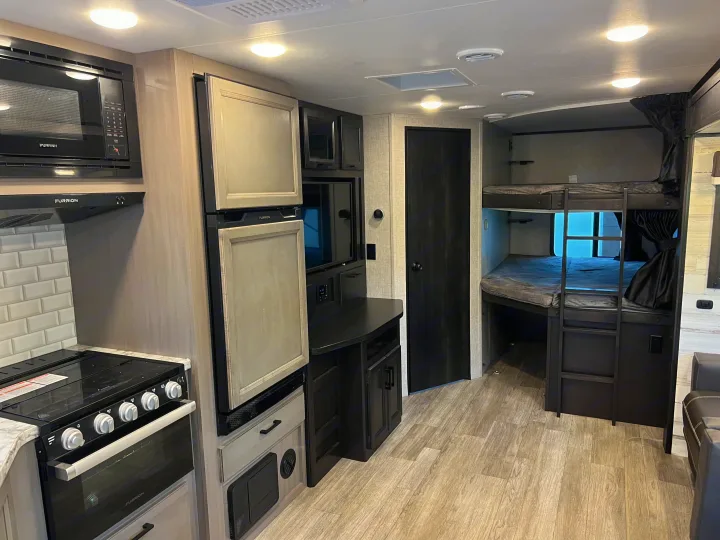 An RV rental interior features a compact kitchen with Furrion appliances, bunk beds, and light wood flooring.. Jayco Jay Feather 2022