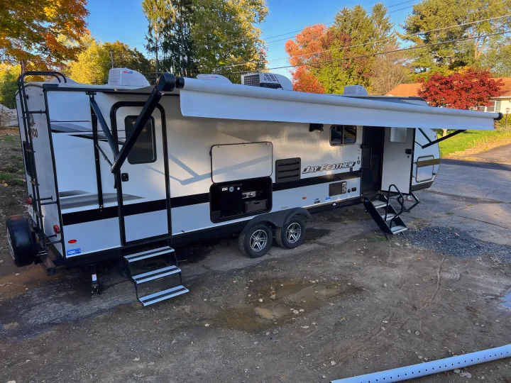 A white Jay Feather travel trailer RV rental, parked with its awning extended, revealing an outdoor kitchen setup.. Jayco Jay Feather 2022