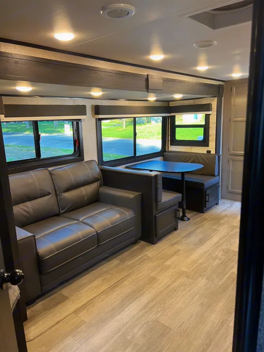 Spacious RV rental interior with a black sofa, dining booth, and large windows offering an outdoor view.. Jayco Jay Feather 2022