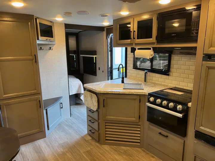 Spacious, modern RV rental interior featuring a full kitchen, dining nook, and glimpse of the bedroom. Ready for adventure!. Jayco Jay Feather 2022
