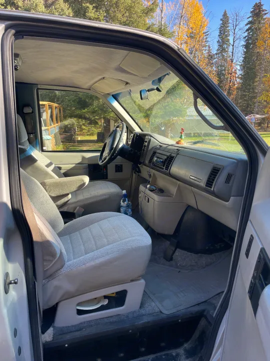 Step into this RV rental: view from the driver's side, featuring front seats, dashboard, and autumn trees outside.. Gmc Custom 1995