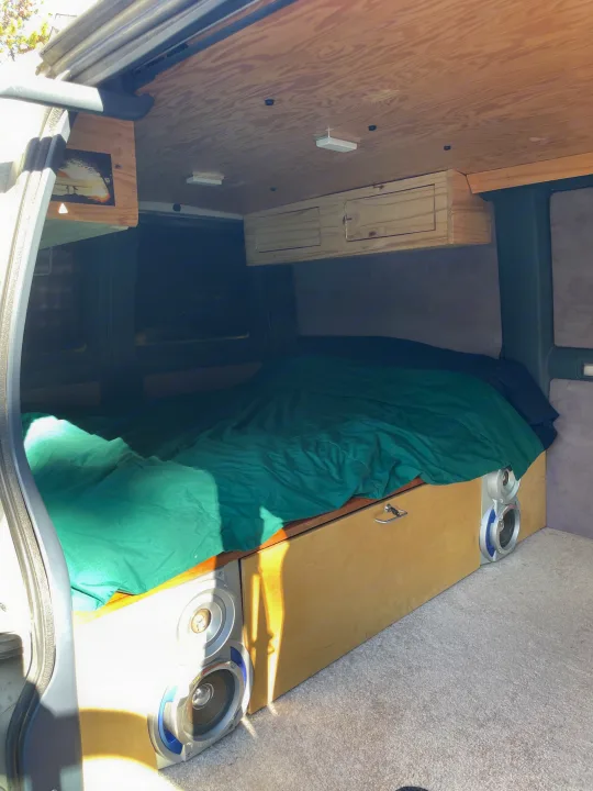 Inside a custom RV rental: wood-paneled interior, a comfy bed with green comforter, built-in speakers, and storage.. Gmc Custom 1995