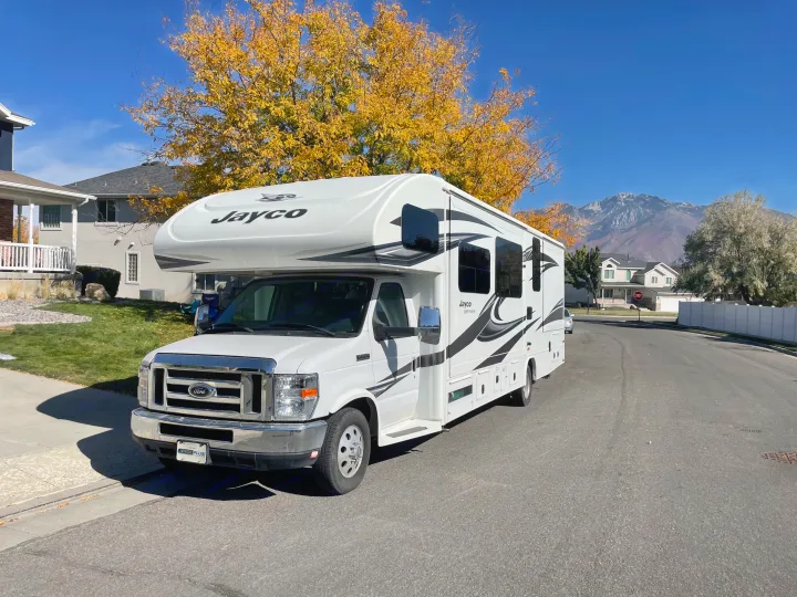 White Jayco Greyhawk RV rental parked on a sunny autumn residential street with golden trees and mountains in the background.. Jayco Greyhawk 2018
